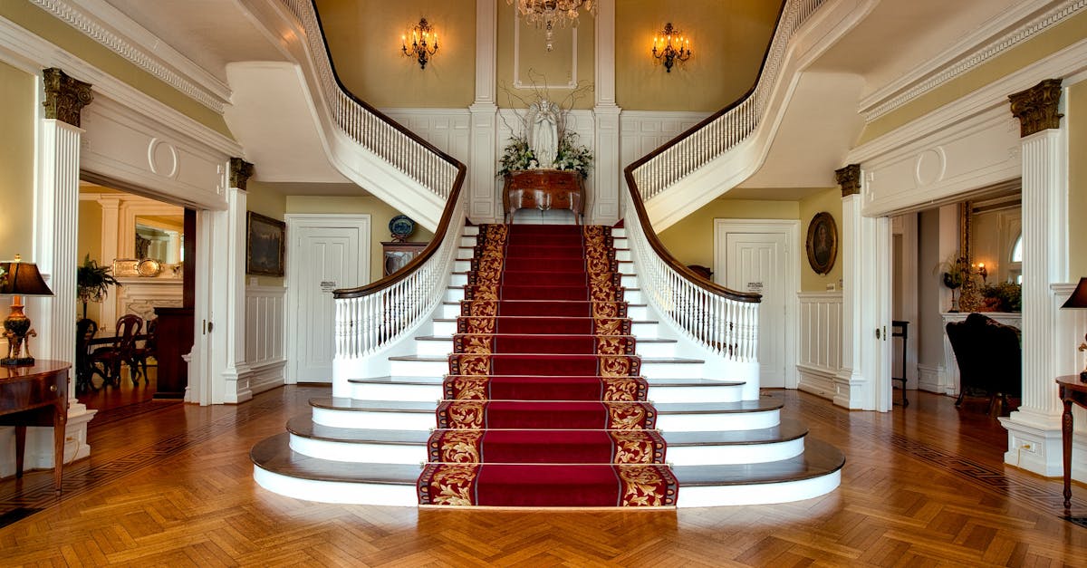 Grand staircase with red carpet in a luxurious hotel lobby, highlighted by a chandelier.
